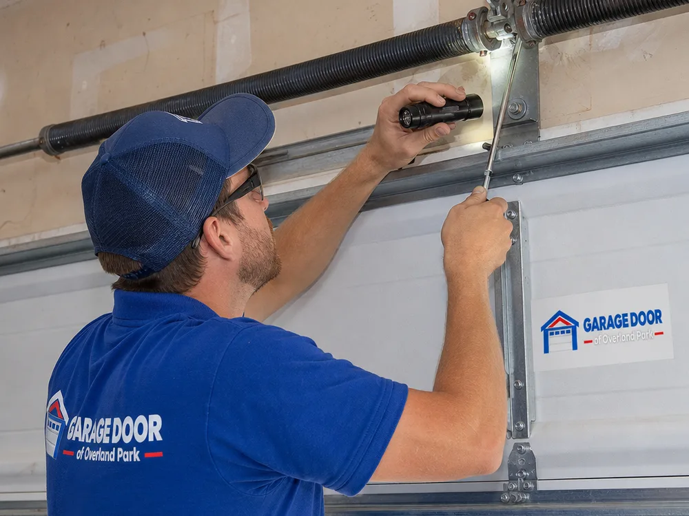 Contractor inspecting garage door torsion springs and center bearing plate with a flashlight and hand tools