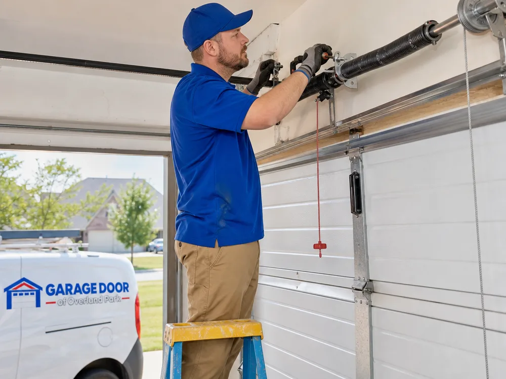 Contractor on a step ladder checking the torsion spring, center bearing plate, and cable drums above a garage door